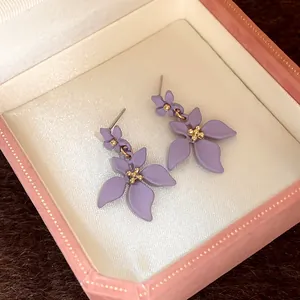 Dettaglio di orecchini a fiore viola opaco con perline dorate in una scatola rosa