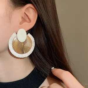 Primo piano di una modella con orecchini a cerchio in rafia bianca intrecciata stile vintage.
