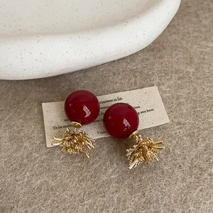 Eleganti orecchini a perno con perla rossa e design a fuochi d'artificio dorati su feltro