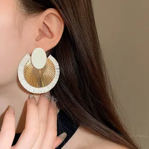 Dettaglio di un orecchino rotondo retrò in rafia con accenti dorati indossato da una modella
