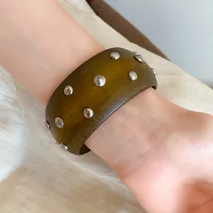 Detailaufnahme eines breiten Holzarmreifs im Vintage-Stil mit runden Silbernieten an einem Handgelenk