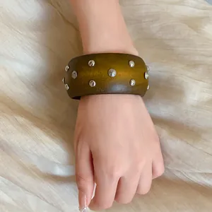 Detailansicht eines breiten Olivenholz-Armreifs mit silbernen Nieten an einem Handgelenk.