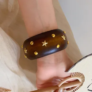 Nahaufnahme eines breiten Holzarmreifs mit goldenen Sternen an einem Handgelenk mit Fächer