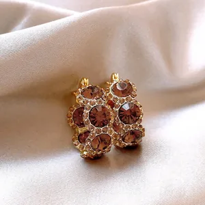 Detailed view of luxury gold-plated hoop earrings featuring brown crystals on satin background