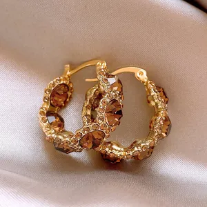 Close-up of gold-plated hoop earrings with sparkling cognac crystals on silk background.