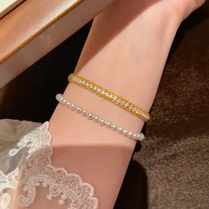 Elegantes goldenes Tennisarmband mit Zirkonia und weißem Perlenarmband am Handgelenk