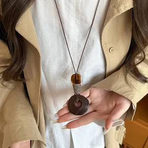 Detailed shot of vintage ethnic circular wood pendant necklace on model wearing beige coat