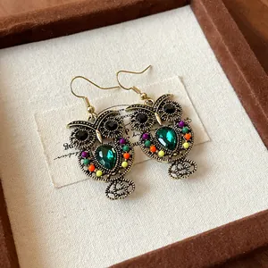 Close-up of vintage bronze owl drop earrings with green teardrop crystal and colorful beads