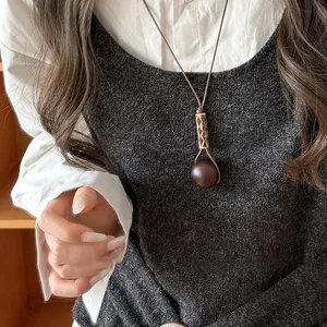 Detailed view of a minimalist vintage round wooden pendant necklace on a grey sweater vest.