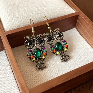 Macro view of detailed vintage owl earrings with green teardrop stones and colorful beads