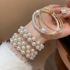 Nahaufnahme eines eleganten zweireihigen Perlenarmbands und eines goldenen Armreifs.