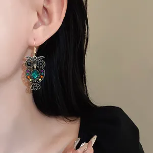 Close-up detail of vintage owl drop earrings with green teardrop crystal on a model.