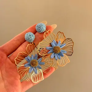 Detailed view of handmade raffia flower earrings in blue and gold for vacation style