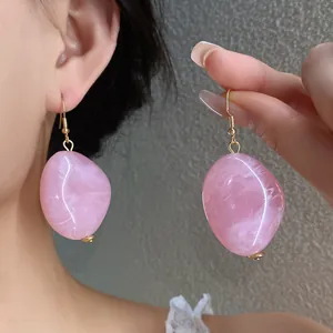 Dettaglio di orecchini pendenti ovali in acrilico rosa marmorizzato indossati