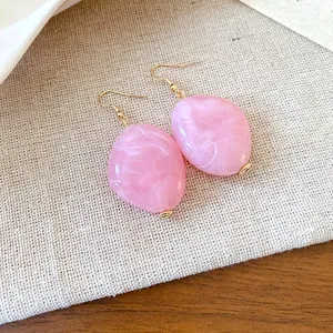 Primo piano di orecchini ovali in acrilico marmorizzato rosa con ganci dorati su lino