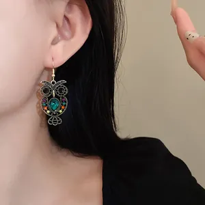 Close-up of vintage owl drop earrings with green teardrop stone and colorful accents