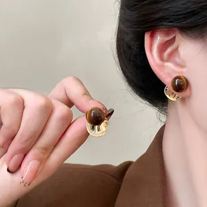 Detail of vintage resin round stud earrings in golden finish and brown cat-eye texture.