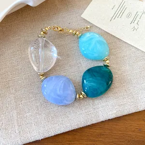 Dettaglio ravvicinato di un bracciale con perle acriliche marmorizzate su sfondo di tessuto.