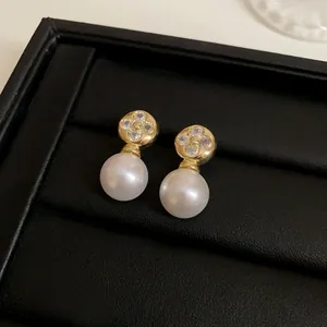 Close-up of French luxury gold flower stud earrings featuring elegant white hanging pearls