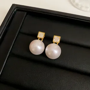 Macro detail of elegant gold-plated stud earrings with square CZ and lustrous pearls.