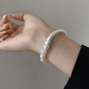 Primo piano di un braccialetto di perle minimalista con design curvo al polso