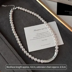 Dettaglio di collana di perle con elemento a tubo curvo argento e prolunga.