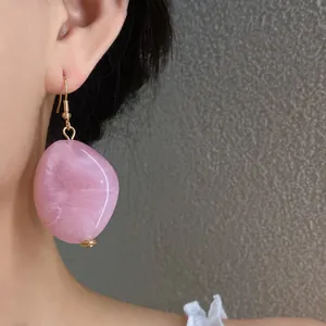Dettaglio ravvicinato di un orecchino ovale in acrilico rosa marmorizzato indossato