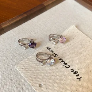 Macro detail of three round cubic zirconia double-layer ear bone clips on textured fabric.