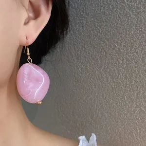 Vista dettagliata di un orecchino ovale in acrilico rosa venato indossato da una modella