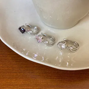 Macro view of three zircon ear cuffs in purple, pink, and white on a ceramic saucer