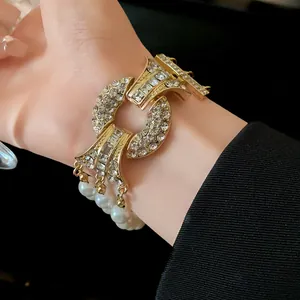 Dettaglio di un elegante bracciale dorato con strass e perle bianche pendenti