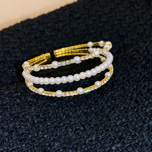 Nahaufnahme eines dreilagigen goldfarbenen Armreifs mit Perlen und funkelnden Strasssteinen