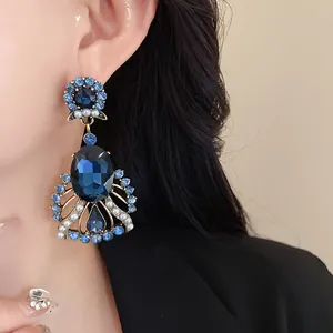 Close-up detail of vintage oversized blue crystal and pearl drop earrings on a model