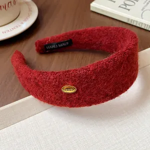 Macro view of a luxury red flocked wide headband with a gold KOREA emblem on a wooden desk.