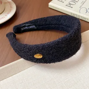 Close-up detail of a minimalist black flocked wide headband with a gold Korea metal tag.
