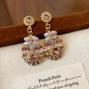 Detailed macro view of elegant pink crystal drop earrings with intricate gold rhinestone accents