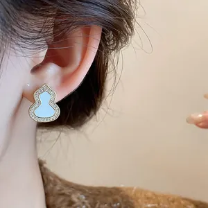 Close-up view of elegant gold gourd earrings featuring white enamel and zircon accents