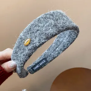 Macro detail of a grey fuzzy wide headband with a small golden 'KOREA' emblem accent.