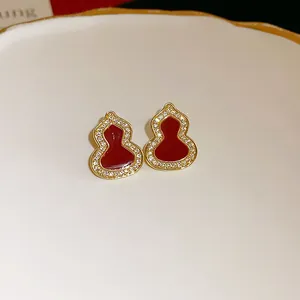 Close-up of elegant red enamel gourd stud earrings with sparkling zircon borders on a white plate
