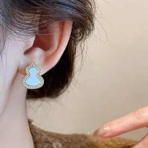 Close-up of elegant gold gourd-shaped earring with white inlay and sparkling zircons