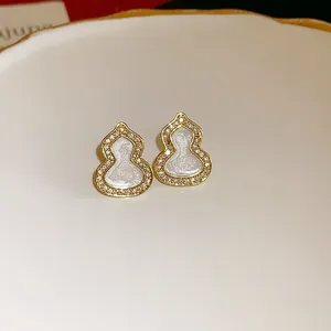 Detailed close-up of gold gourd stud earrings with white enamel and sparkling zircons