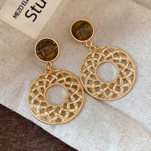 Detailed macro view of vintage gold hollow-out drop earrings featuring tiger eye stone