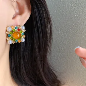 Close-up of vintage square stud earrings with pearls and rhinestones on a female ear.