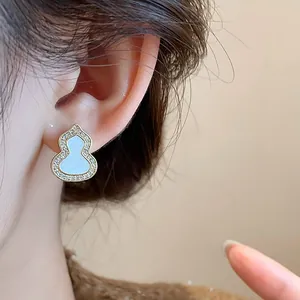Elegant gold gourd stud earrings with white enamel and sparkling zircons on model ear