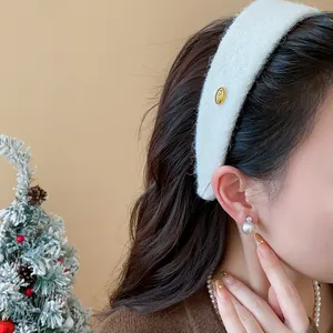 Close-up view of a white flocked wide headband with a gold emblem on a model wearing earrings.