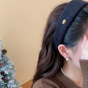 Close-up of a wide black flocked headband with a gold emblem on a female model.