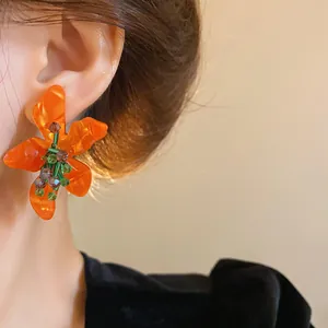 Close-up view of bright orange acetate flower earring with crystal details worn on ear