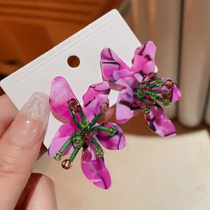 Close-up of pink acetate flower earrings featuring intricate green crystal bead stamens.