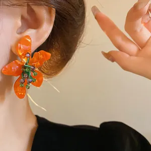 Detailed close-up of vibrant orange flower-shaped earrings made of translucent acetate.