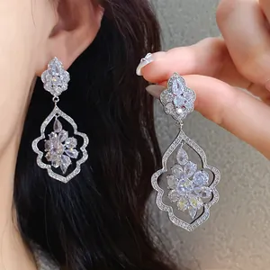 Close-up of sparkling zircon dangle earrings with intricate leaf and floral patterns.